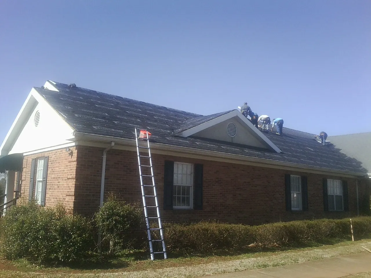 Crew tearing shingles off a brick ranch roof with a ladder set — Emergency Roof Repair work by our crew in Pennsylvania Furnace
