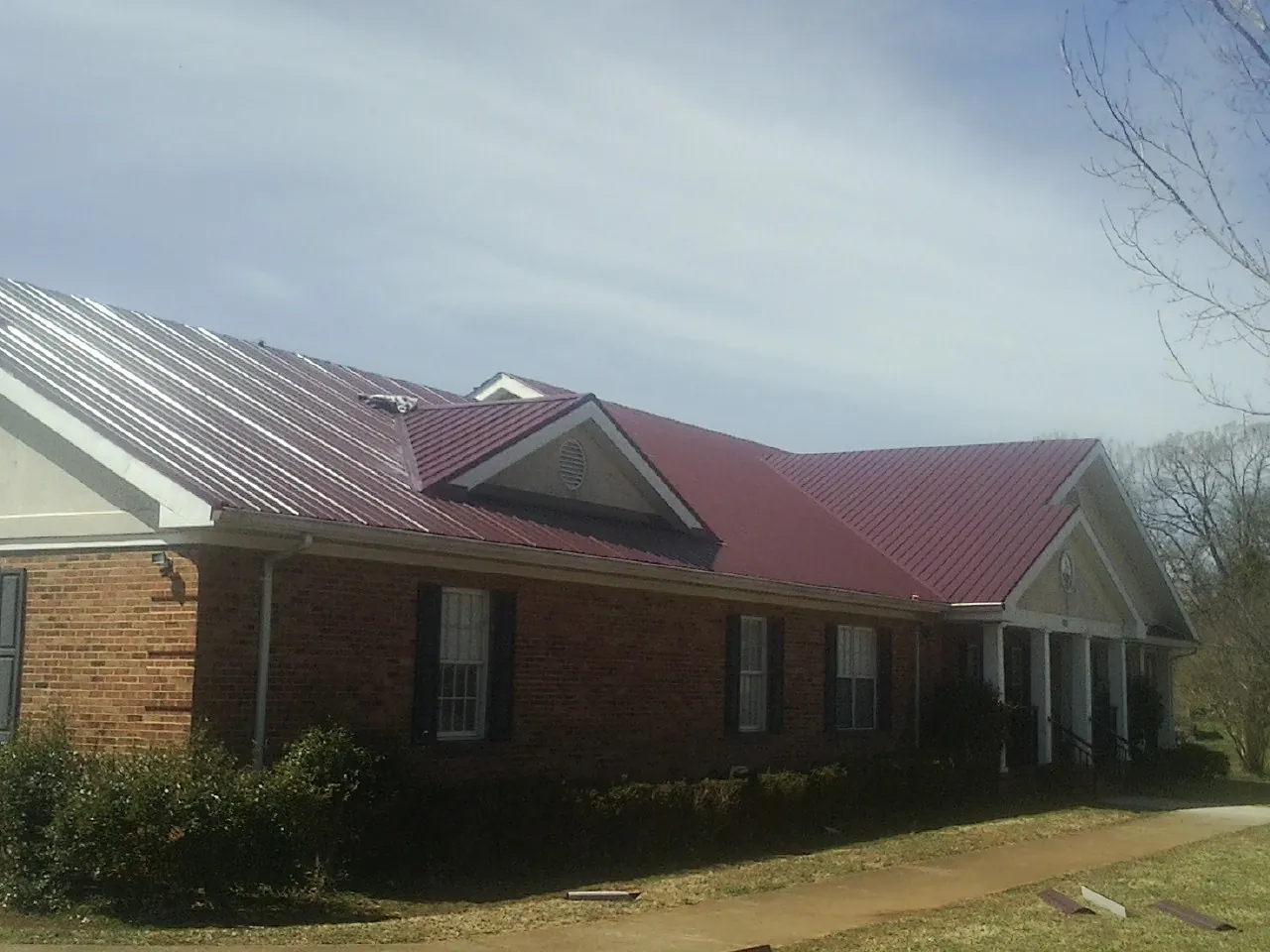 Red metal roof with gabled entries on a long brick building, from a Hail Damage Roof Repair job in Pennsylvania Furnace