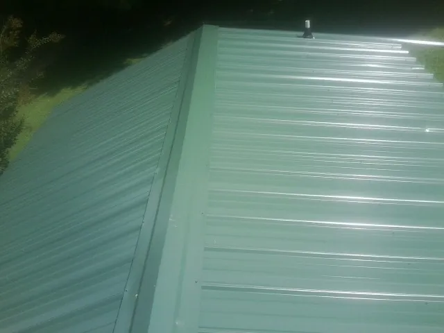 New green metal panels meeting at the ridge of a roof — Flat Roof Repair work by our crew in Pennsylvania Furnace