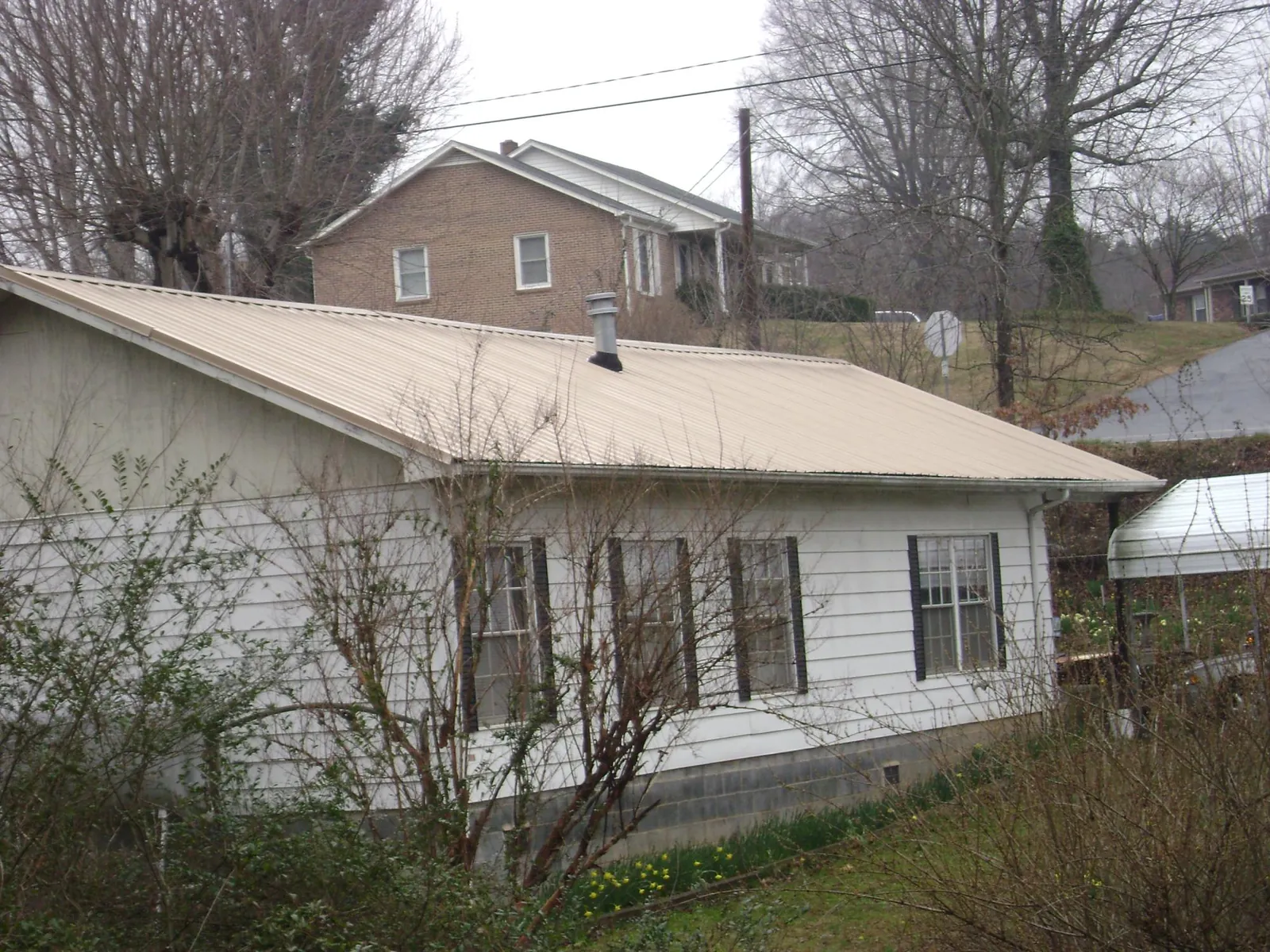 Tan metal roof on a white sided house set into a hillside — Commercial Roofing by Roofing Brothers in Pennsylvania Furnace
